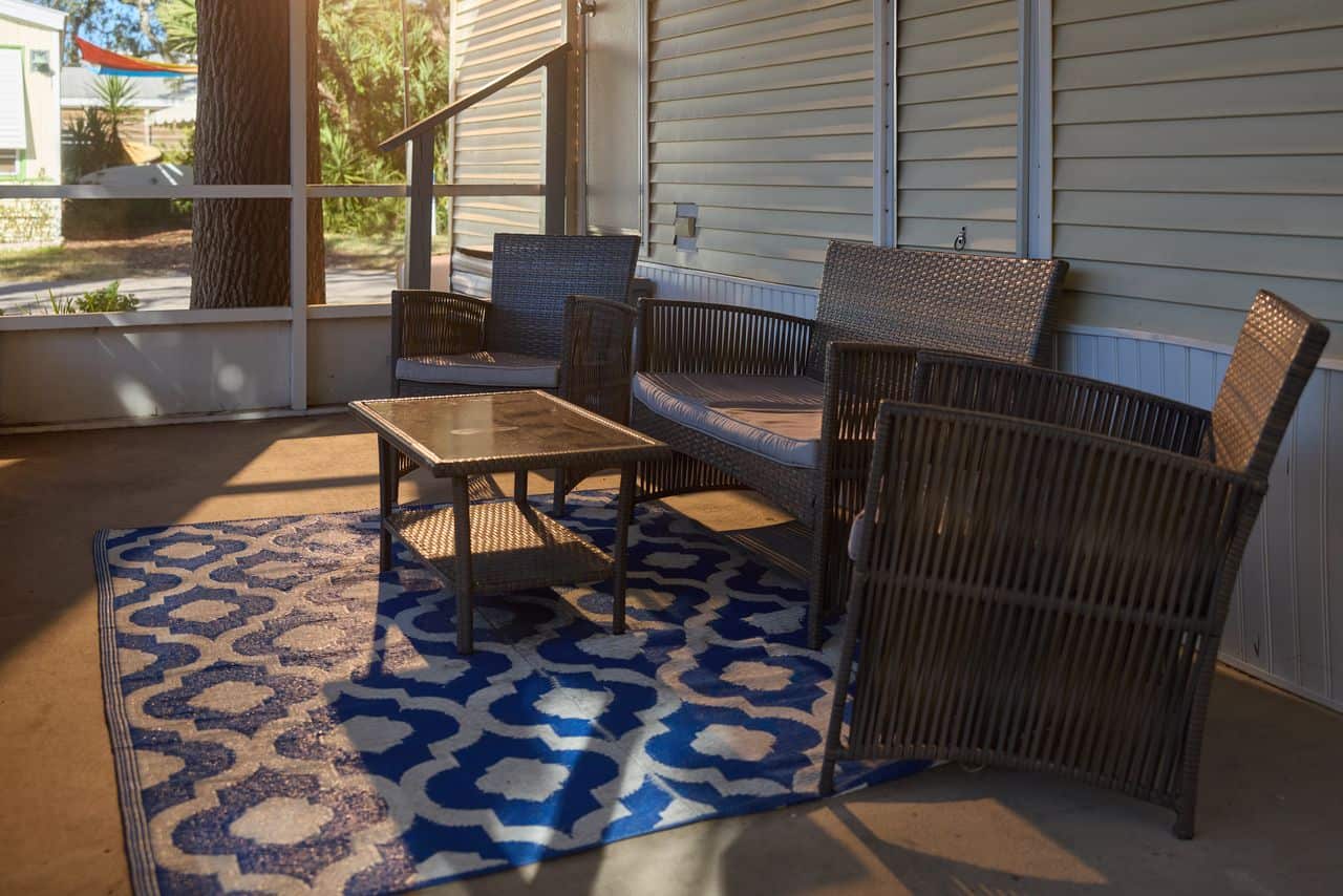 Outdoor patio with wicker furniture set, including two chairs, a loveseat, and a glass-top table, arranged on a blue and white patterned rug.