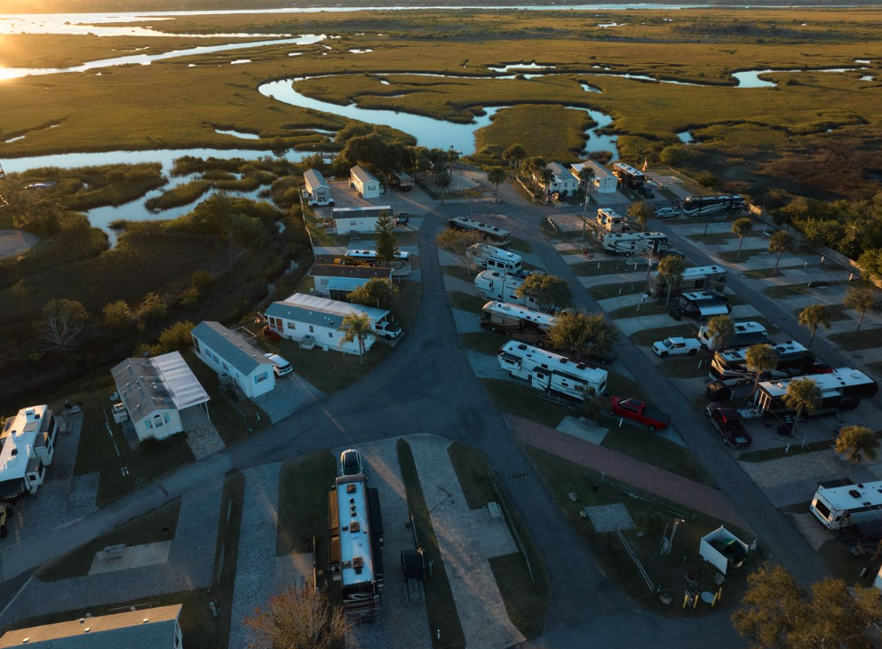 Aerial view of an RV park bordering a coastal marsh at sunset.